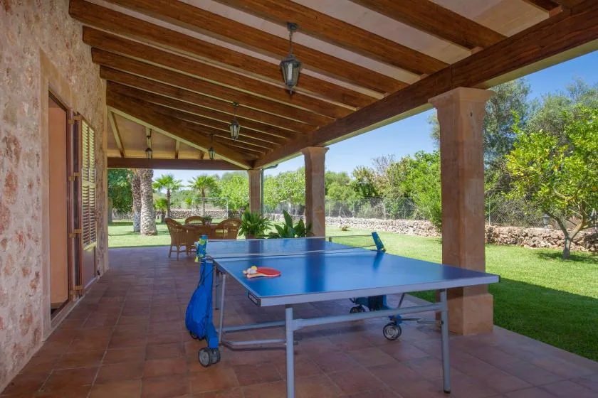 A covered patio with a table tennis table overlooking a garden.