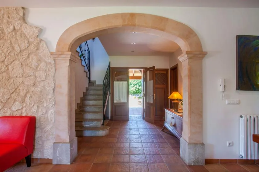 An arched entryway opens onto a tiled hall with a staircase and open doors.