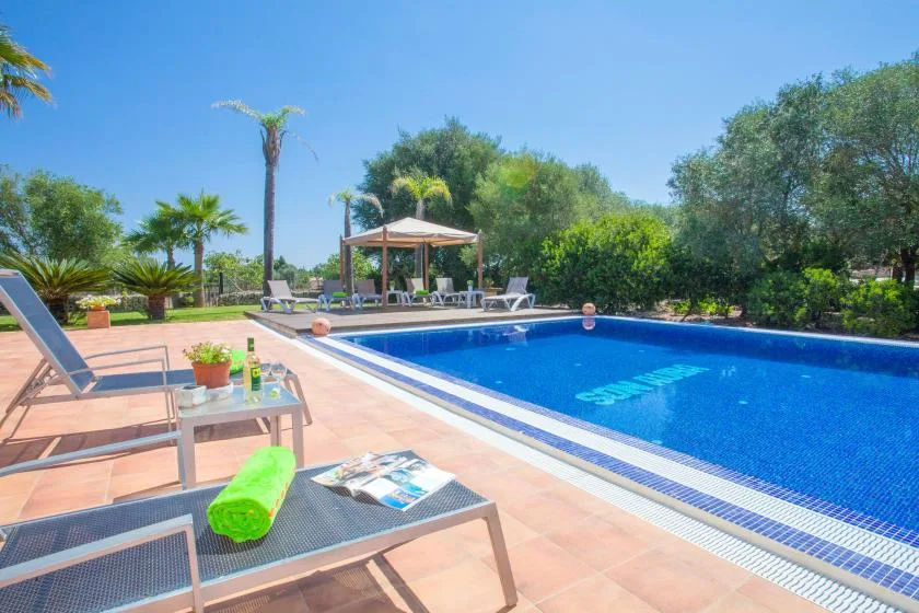 A swimming pool beside a tiled deck with loungers and a shaded gazebo.