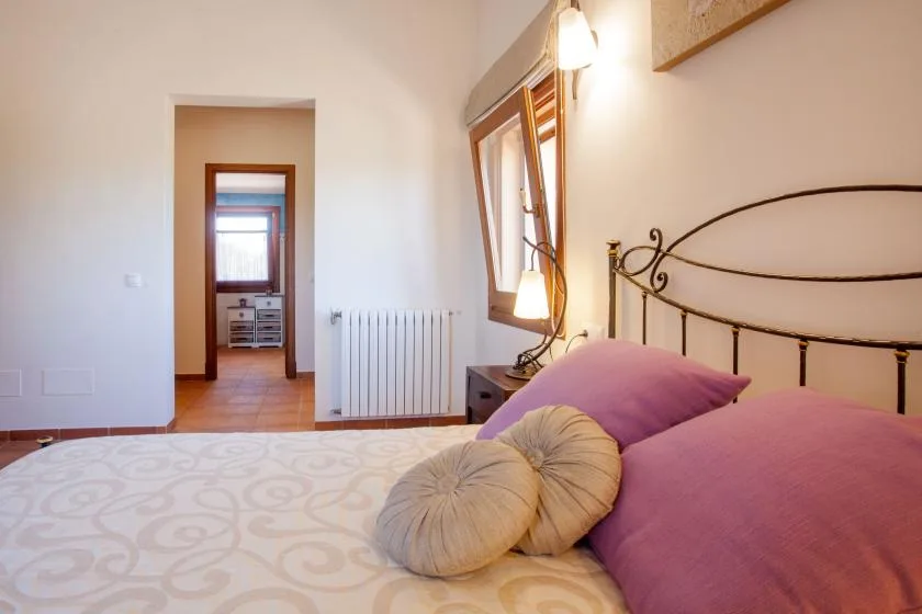 A bedroom with a patterned bedspread, pillows, and a window beside the bed.