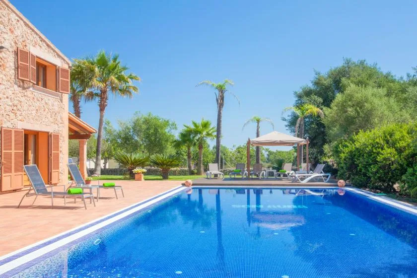 An outdoor swimming pool beside a stone house, with lounge seating and greenery.