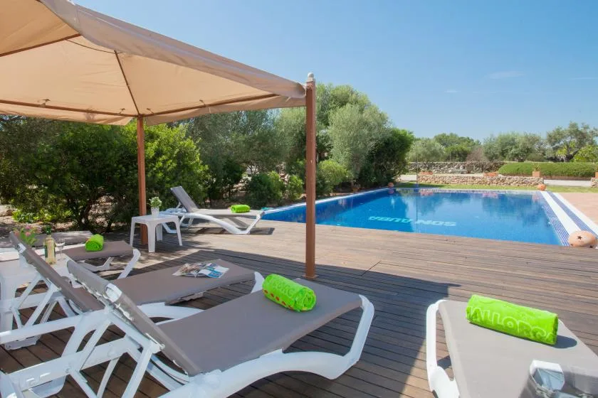 A swimming pool beside a wooden deck with lounge seating under a sunshade.
