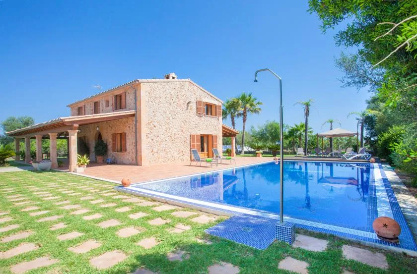 A stone house stands beside a swimming pool and grassy patio.