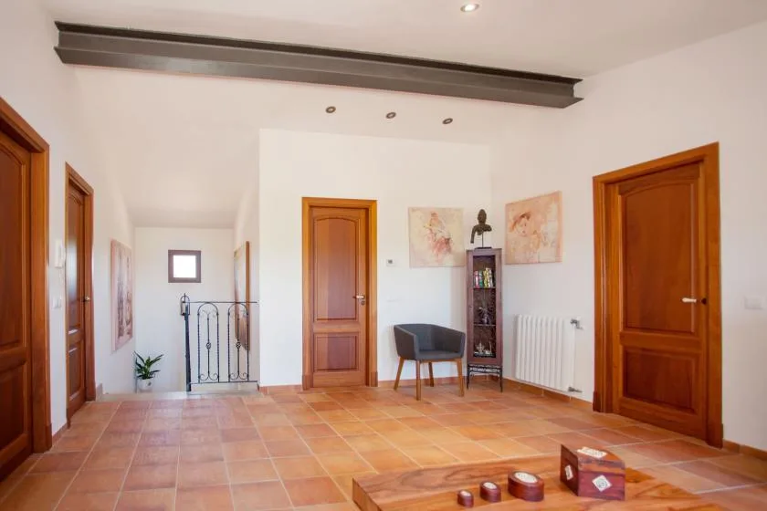 A bright interior hallway with wooden doors, tiled flooring, and a small seating area.