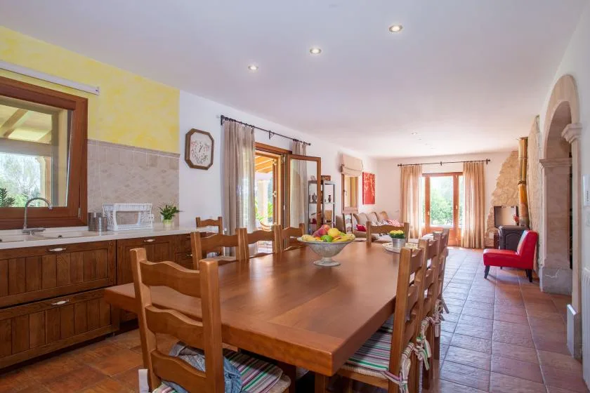 A dining area with a long wooden table and chairs beside a kitchen counter.