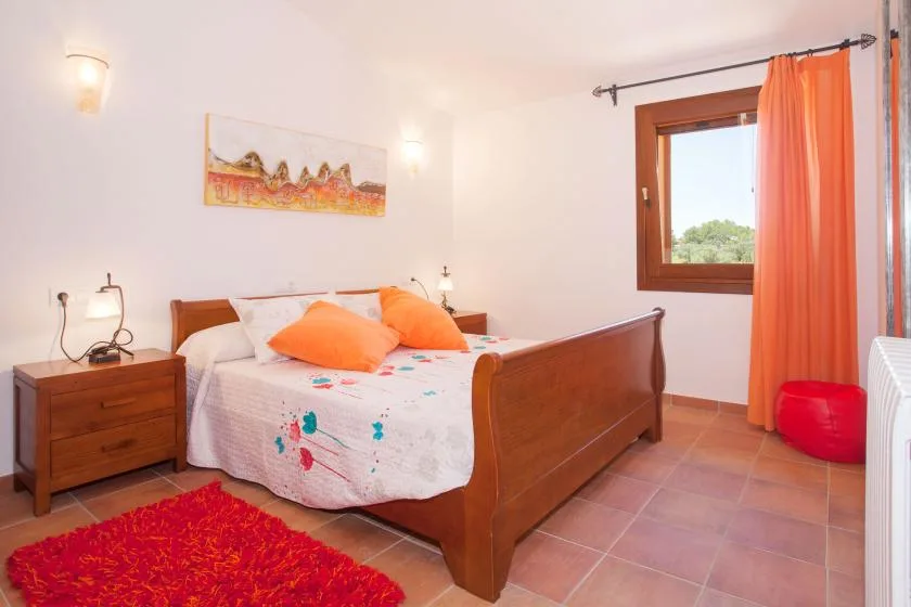 A bedroom with a wooden bed, colorful bedding, and orange curtains by the window.