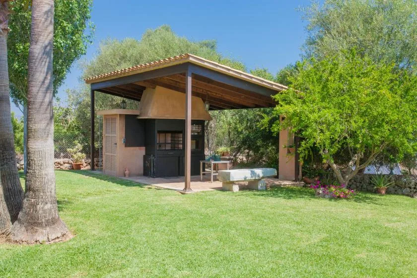 A covered outdoor patio with a built-in grill and a lawn.