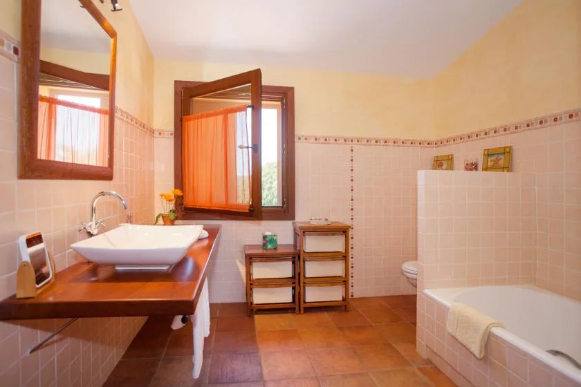 A tiled bathroom with a bathtub, sink, and an open window.