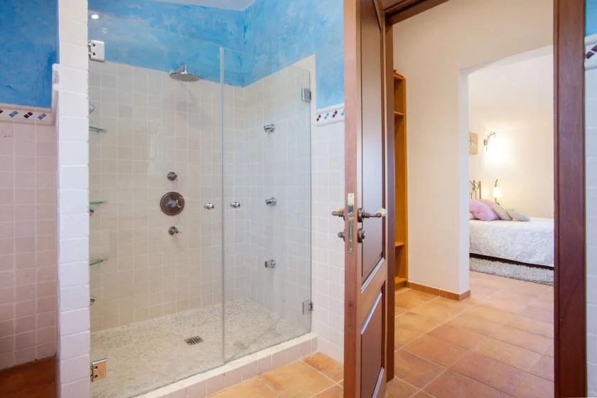 A tiled bathroom with a glass shower beside an open doorway.
