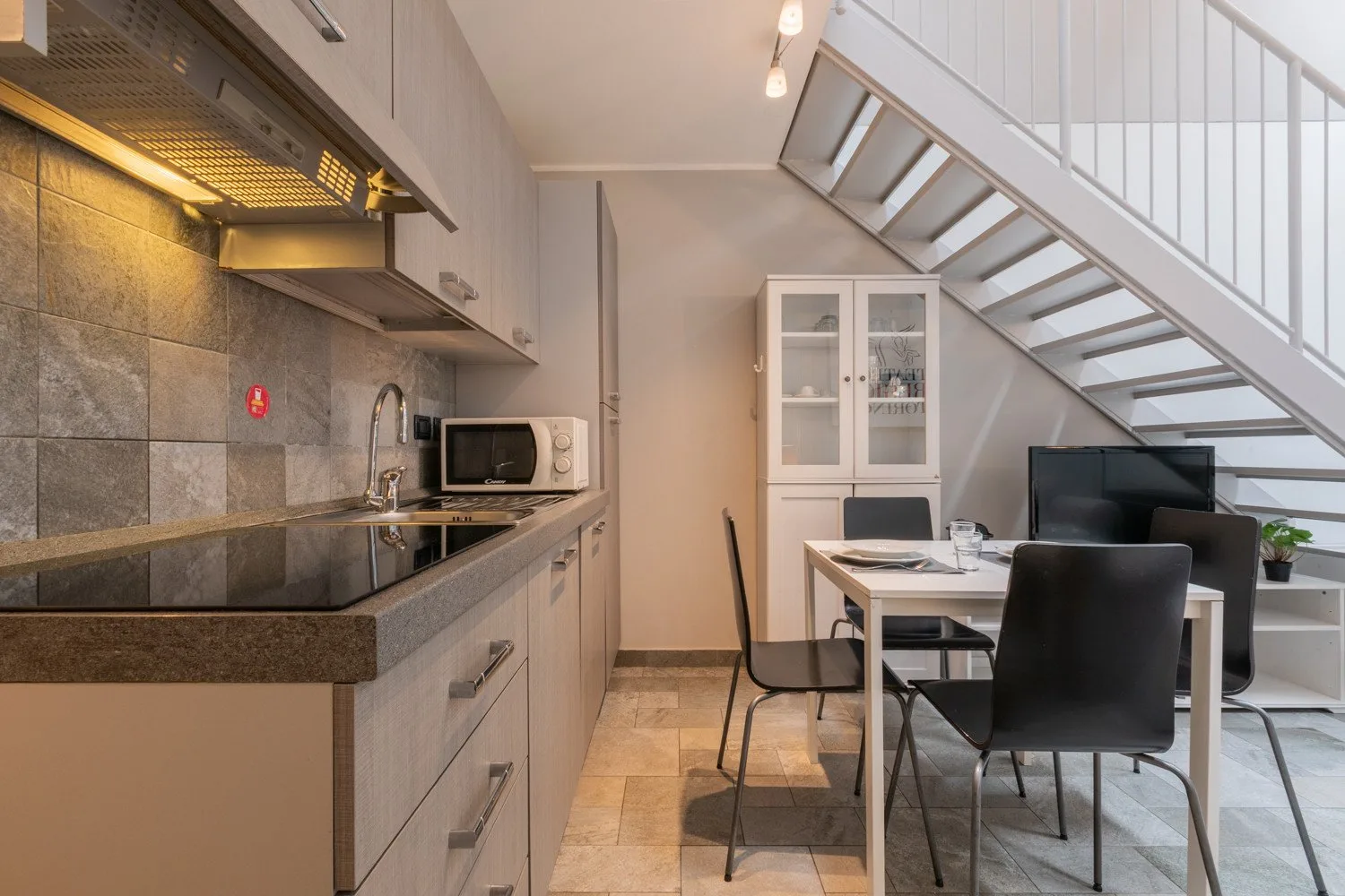 Una cocina moderna y zona de comedor con una mesa bajo una escalera abierta.