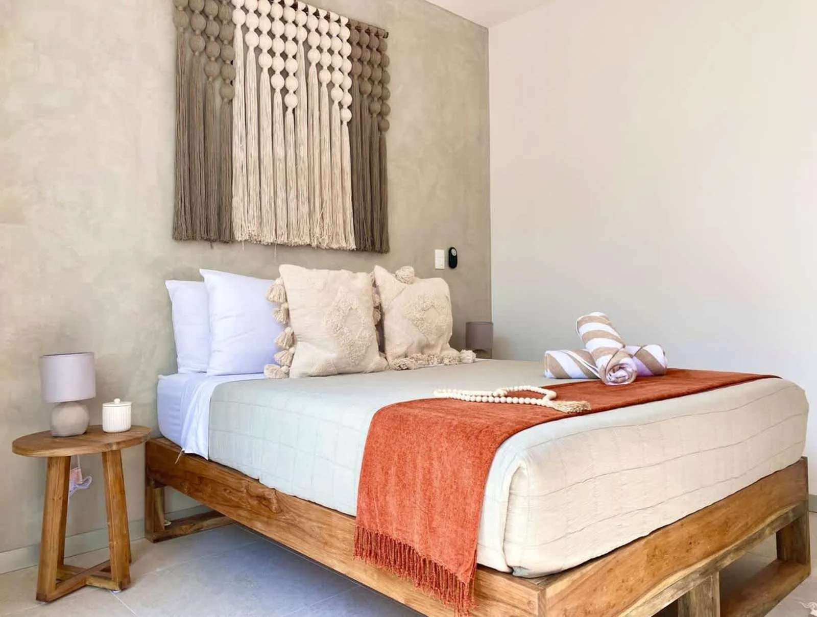 Un dormitorio con una cama vestida con ropa de cama clara y una manta color óxido.