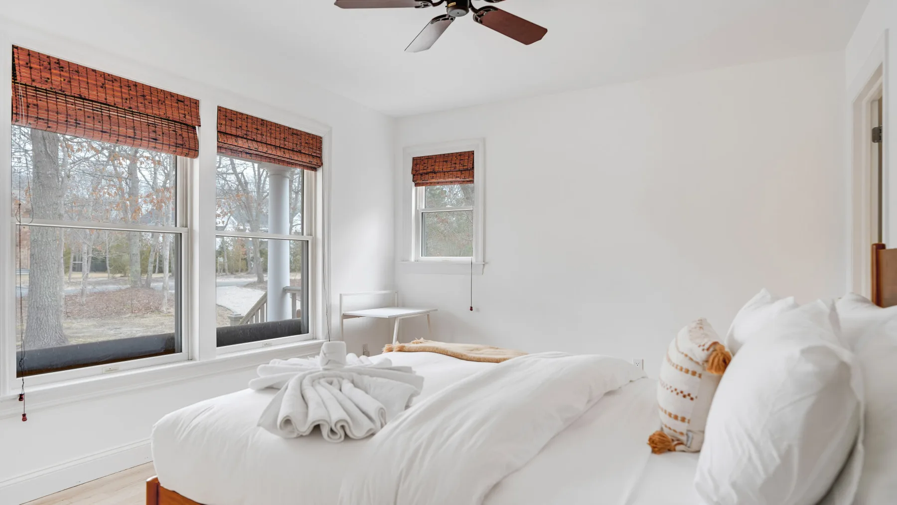 Un dormitorio luminoso con una cama bien tendida y ventanas con persianas tejidas.