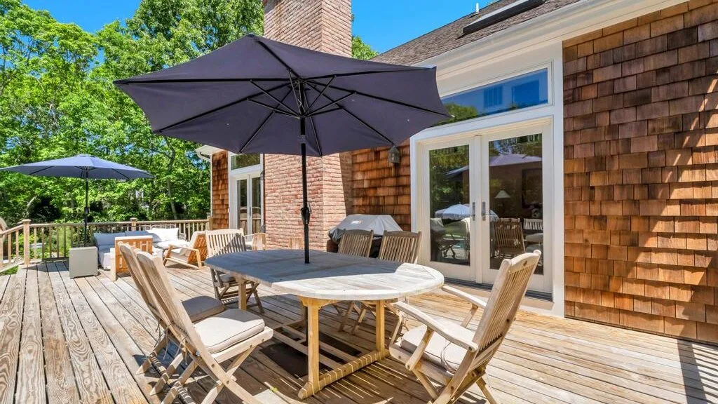 Un patio de madera con una mesa de comedor al aire libre, asientos y una sombrilla grande.