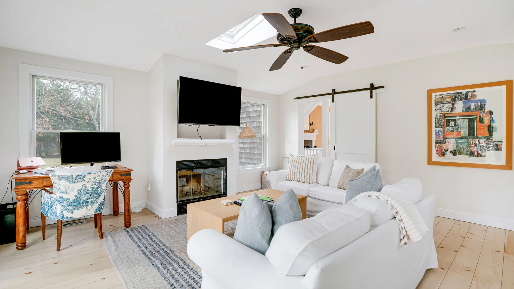 Una sala luminosa con asientos blancos, una chimenea y un ventilador de techo.