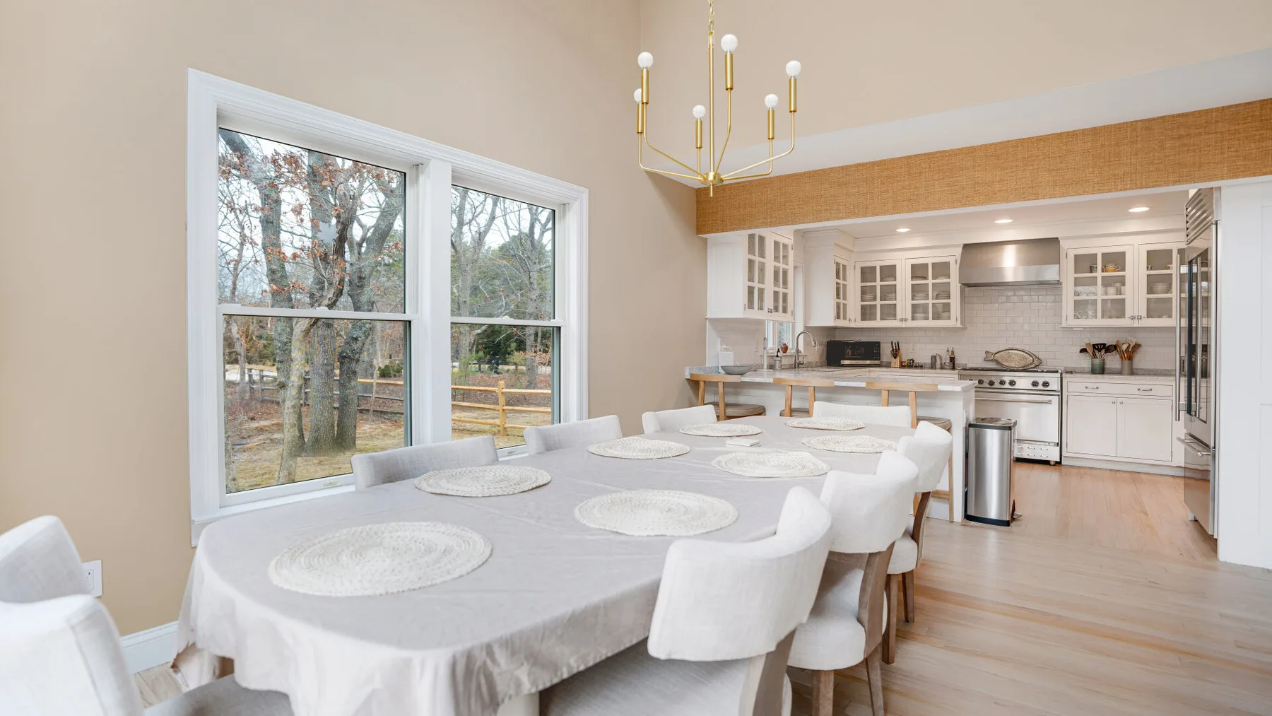 Un comedor con una mesa larga junto a grandes ventanas y una cocina abierta.