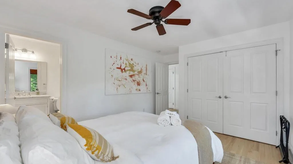 Un dormitorio luminoso con ropa de cama blanca y una obra abstracta en la pared.