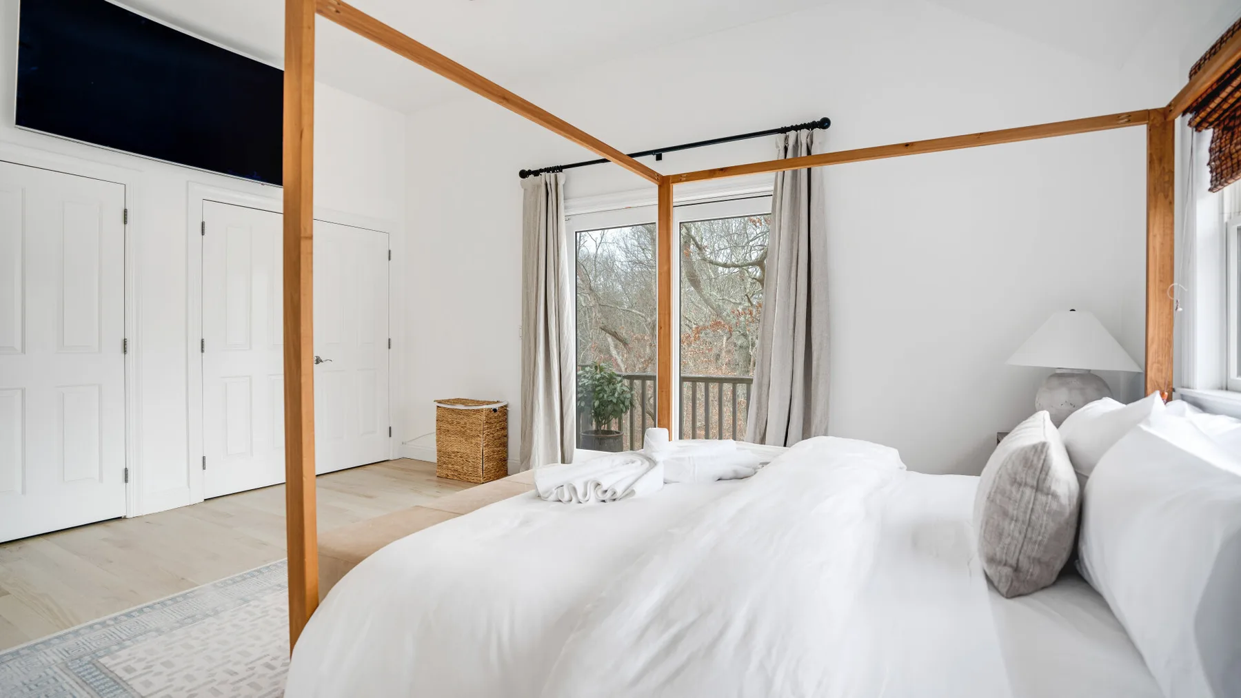 Un dormitorio luminoso con cama con dosel y grandes ventanas con vistas a los árboles.