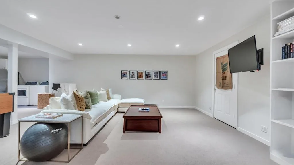 Una sala luminosa con sofá seccional, mesa de centro y televisor montado en la pared.