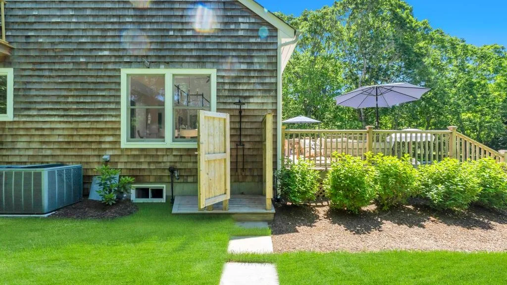 El exterior de una casa da a una terraza de madera con sombrilla y jardín.