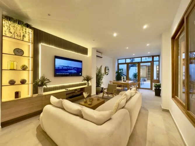 Una sala de estar luminosa con asientos color crema y un televisor en la pared.
