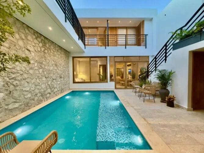 Una piscina en un patio está junto a un muro de piedra y un edificio moderno.