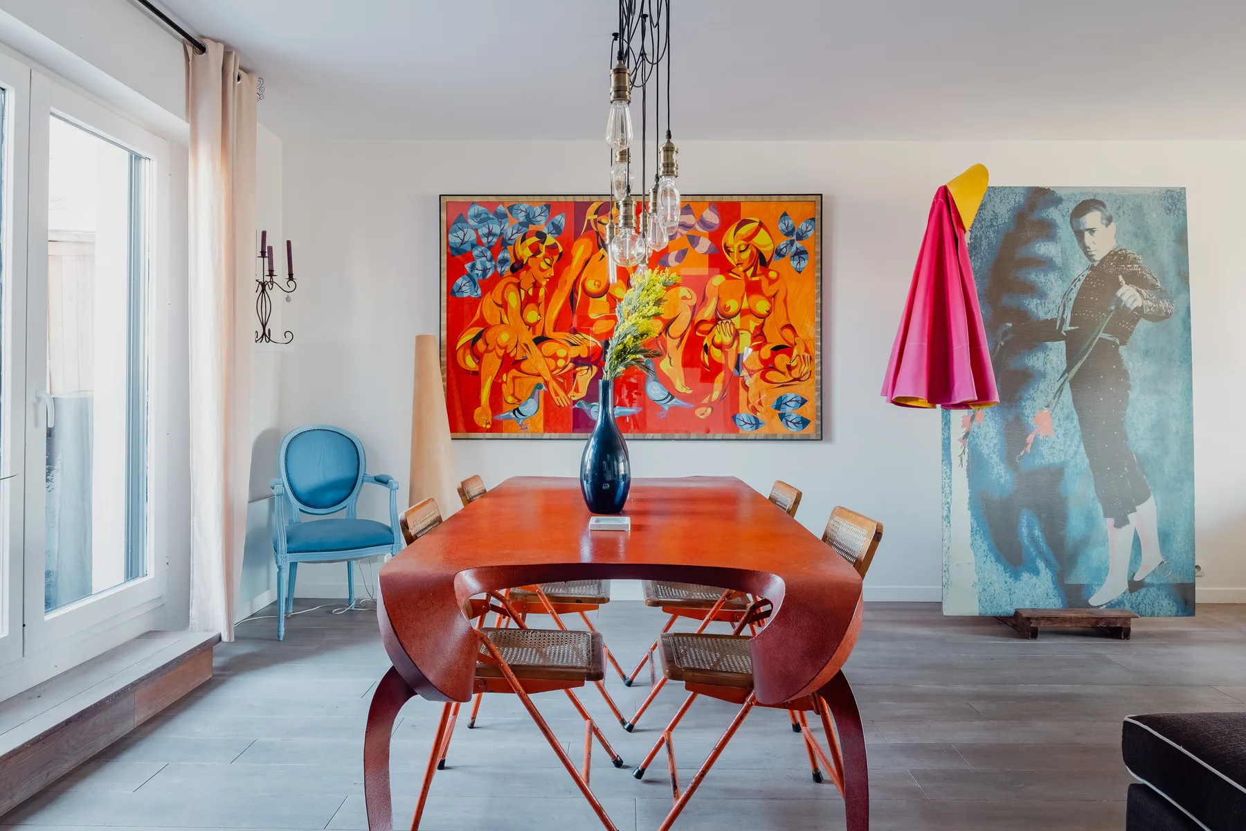 A dining room with a long table, chairs, and colorful artwork on the walls.