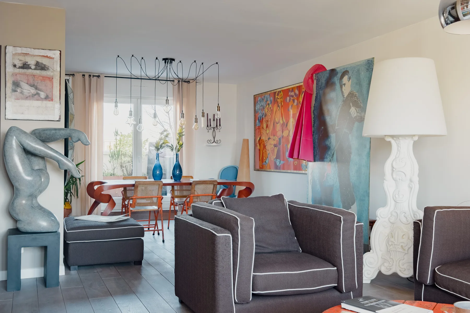 A living room with seating, colorful artwork, and a dining area by the window.