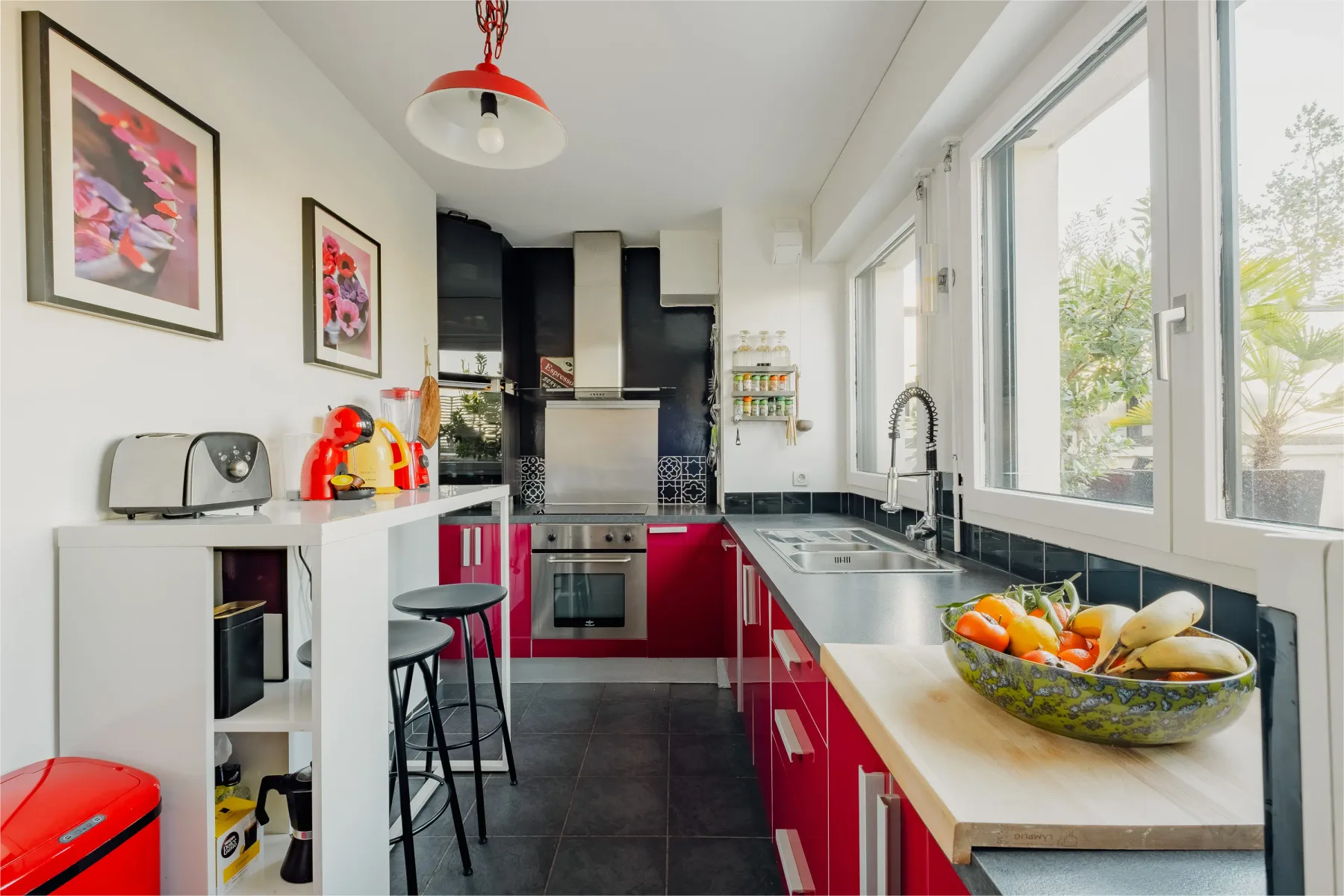 A bright kitchen with red cabinets, dark flooring, and large windows.