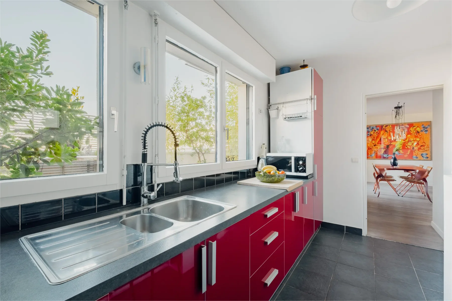 A bright kitchen with red cabinets, a sink, and large windows.