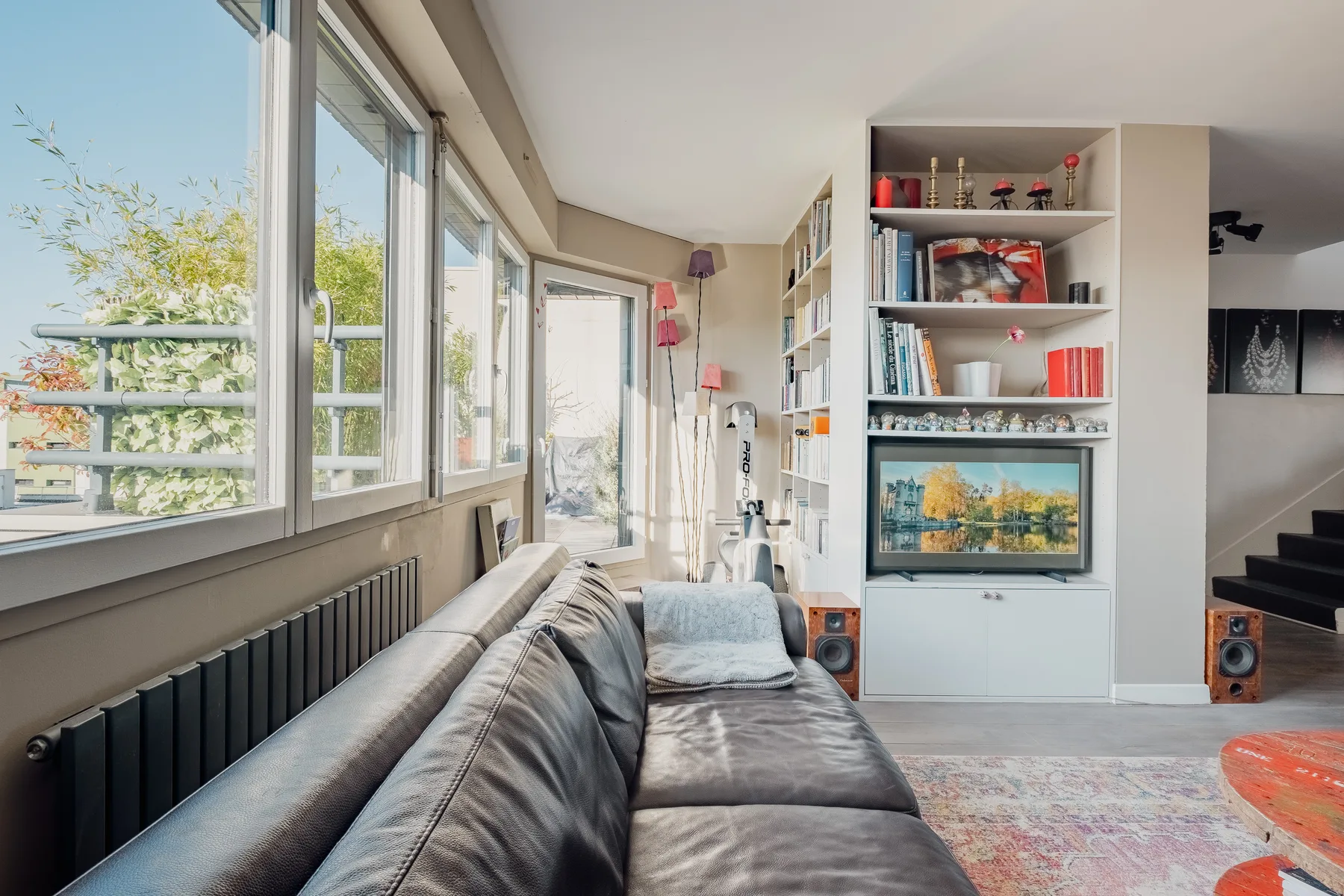 Living room with a long seating area beside large windows and built-in shelving.