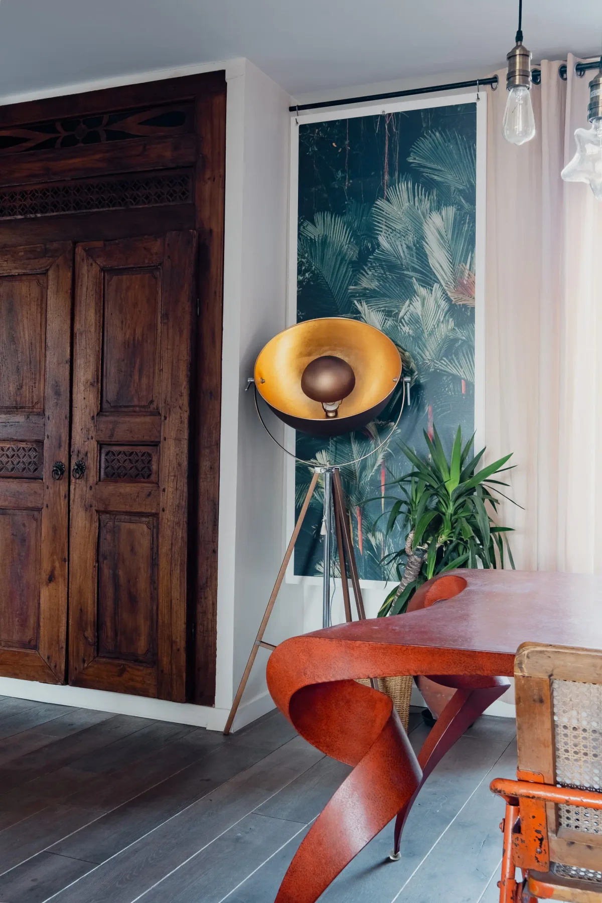 A dining area with a sculptural wooden table beside a tall leafy plant.