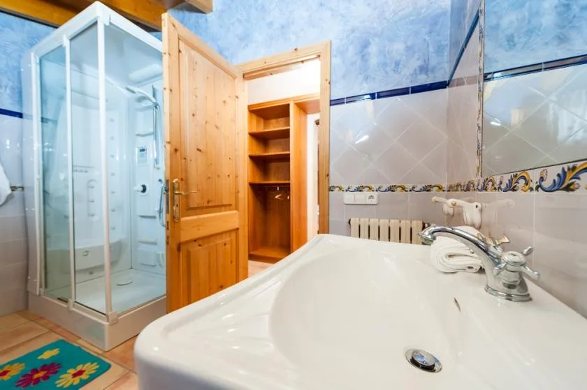 Un baño con ducha de vidrio, lavabo y puerta de madera abierta.