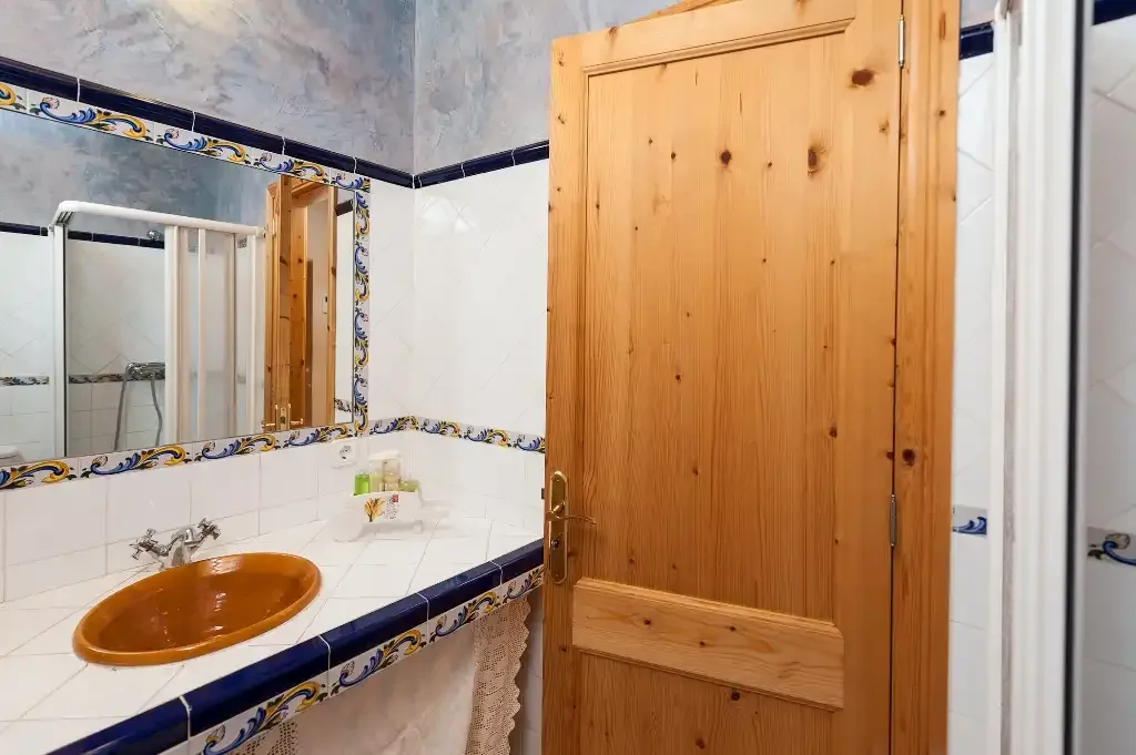 Un baño con lavabo, espejo y puerta de madera.