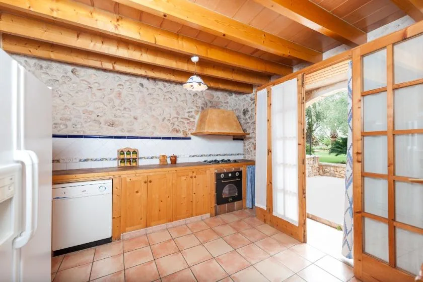 Una cocina con armarios de madera, suelo de baldosas y una puerta acristalada abierta.
