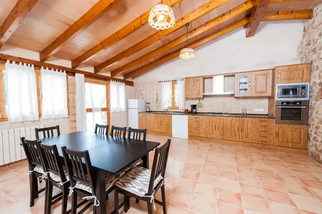 Comedor y cocina con una mesa larga bajo vigas de madera vistas.