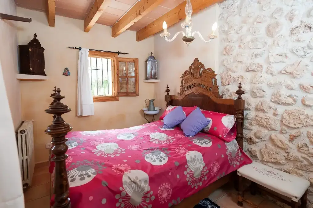 Un dormitorio con una cama colorida junto a una pared de piedra.