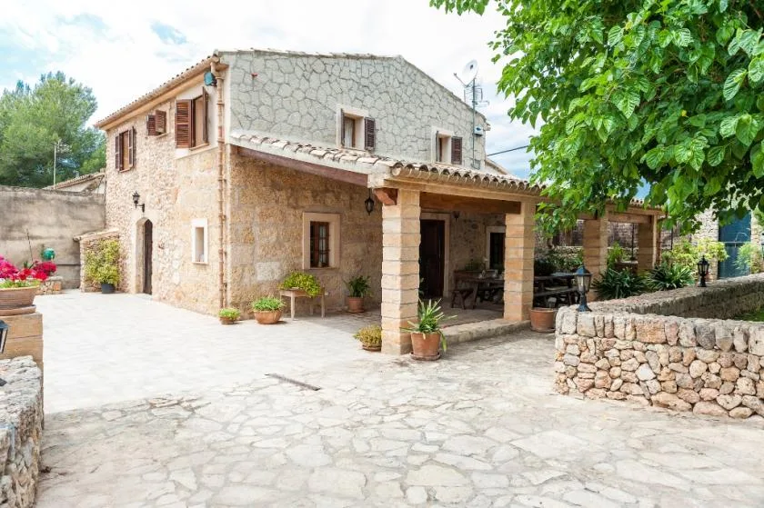 Una casa de piedra da a un patio pavimentado con una zona cubierta para sentarse al aire libre.