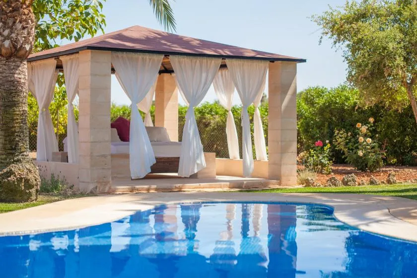 Una piscina está junto a un pabellón de jardín con cortinas.