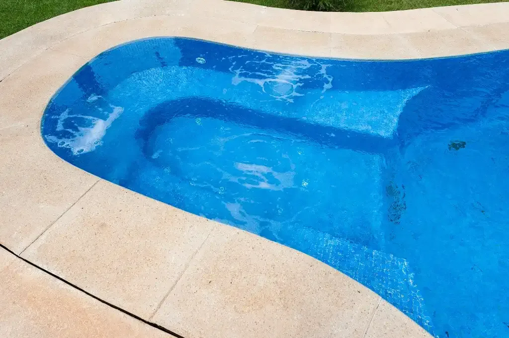 Una piscina de agua azul está rodeada por una terraza de piedra clara.