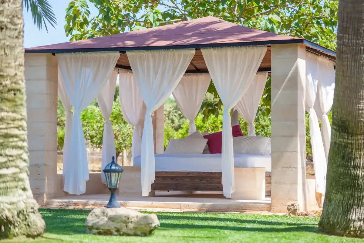 Una cabaña al aire libre con una cama acolchada y cortinas blancas sueltas.
