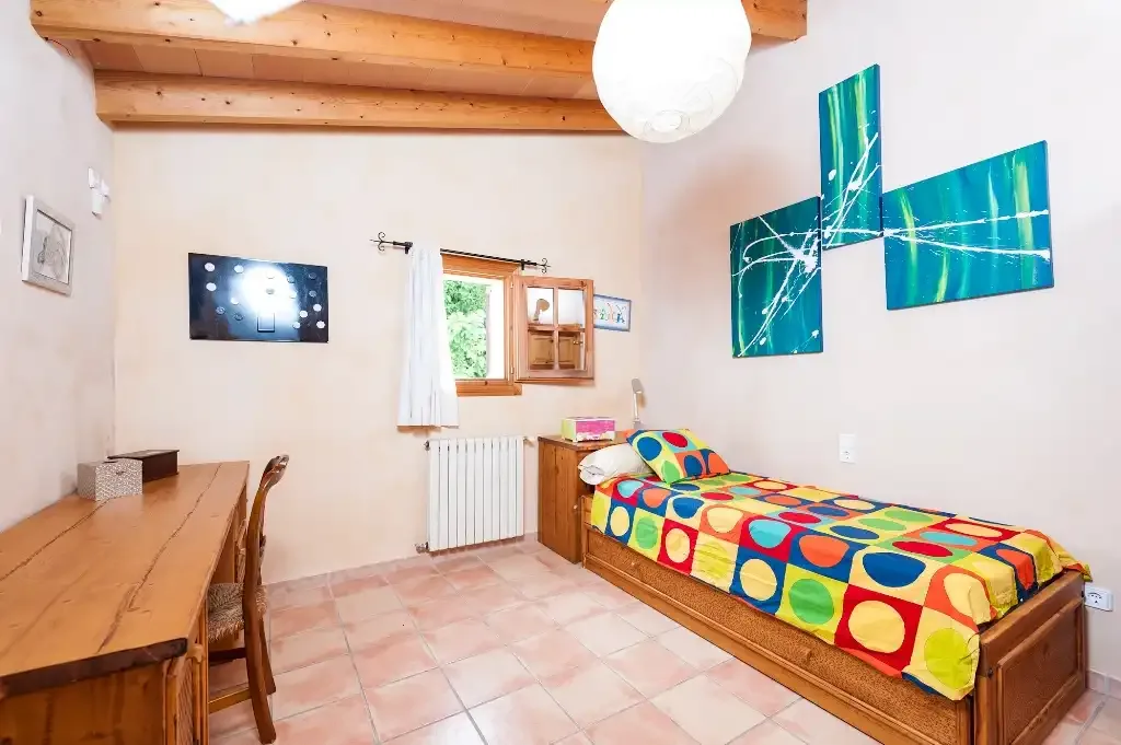 Un dormitorio con una cama individual, un escritorio y ropa de cama colorida.