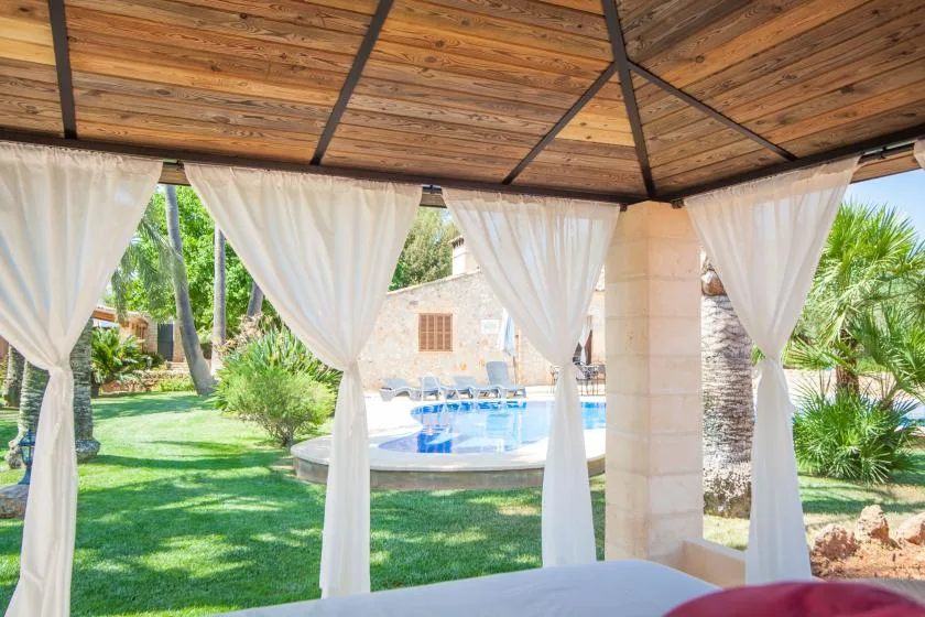 Una zona de estar exterior a la sombra da a una piscina y un jardín cuidado.