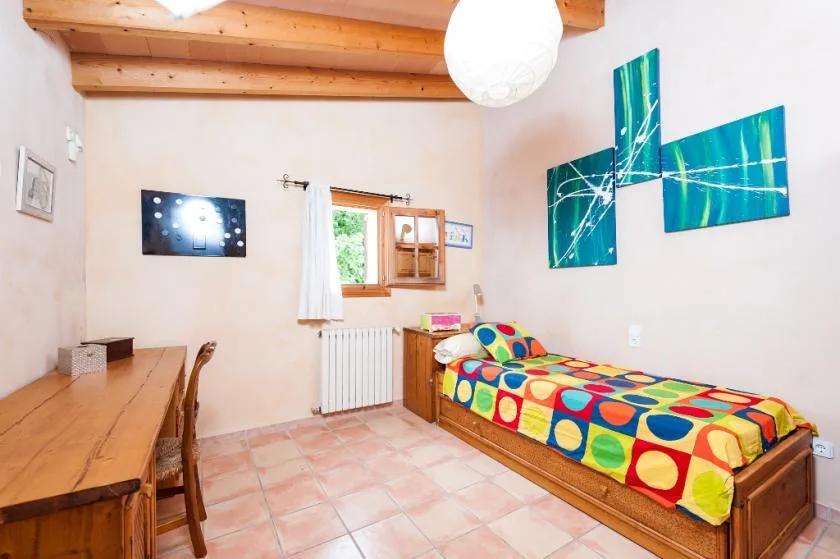 Un dormitorio colorido con una cama individual, vigas de madera y suelo de baldosas.