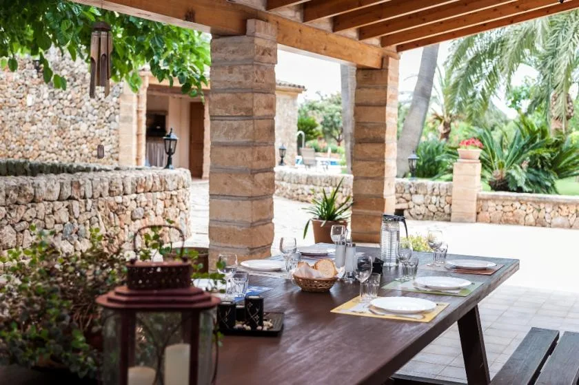 Un comedor exterior cubierto con una mesa puesta junto a un muro de piedra.