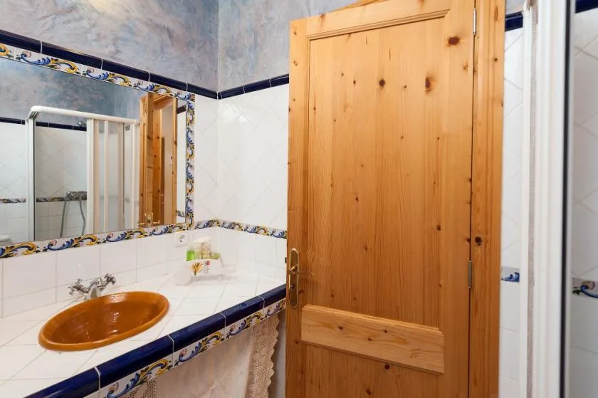 Un lavabo de baño alicatado con espejo en la pared y puerta de madera.
