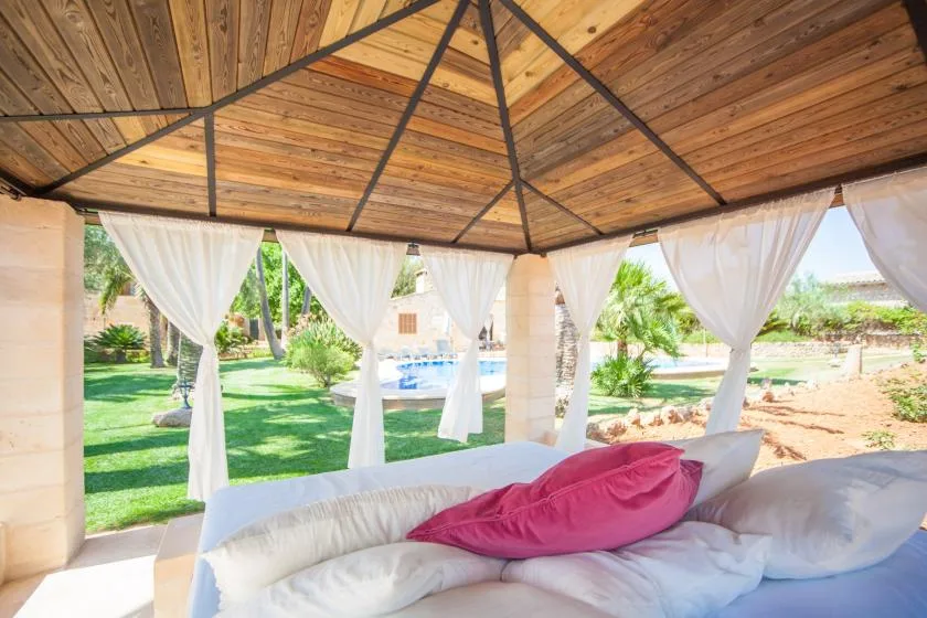 Un salón exterior a la sombra da a un jardín y una piscina.
