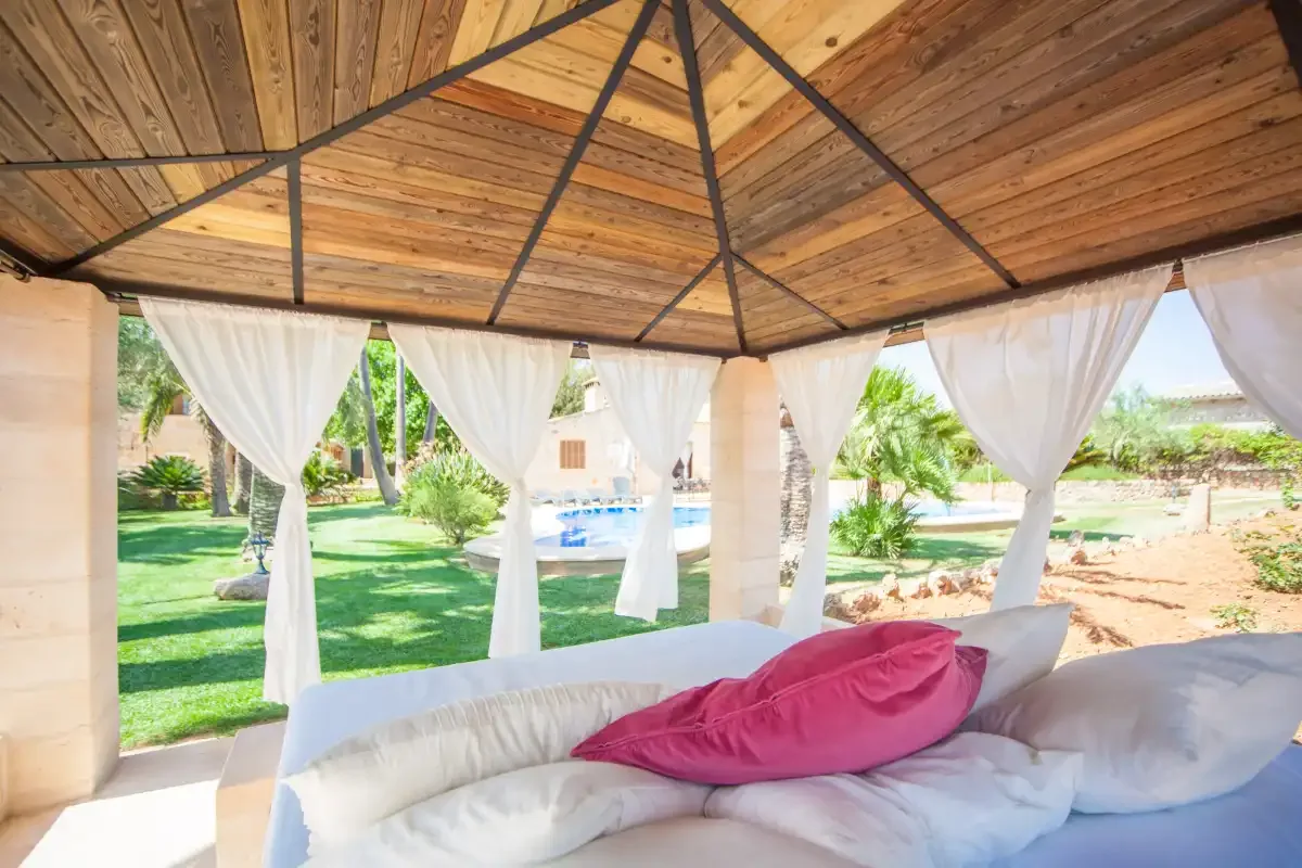 Una zona de estar cubierta al aire libre da a un jardín y una piscina.