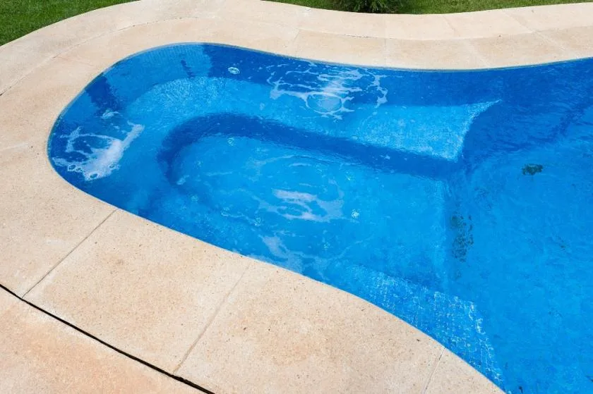 Una piscina con una terraza de piedra clara y agua burbujeando en el borde.