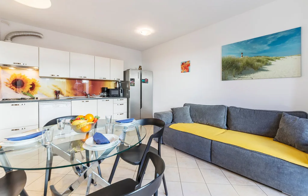 Un espacio diáfano y luminoso con cocina, mesa de comedor de cristal y asientos grises.