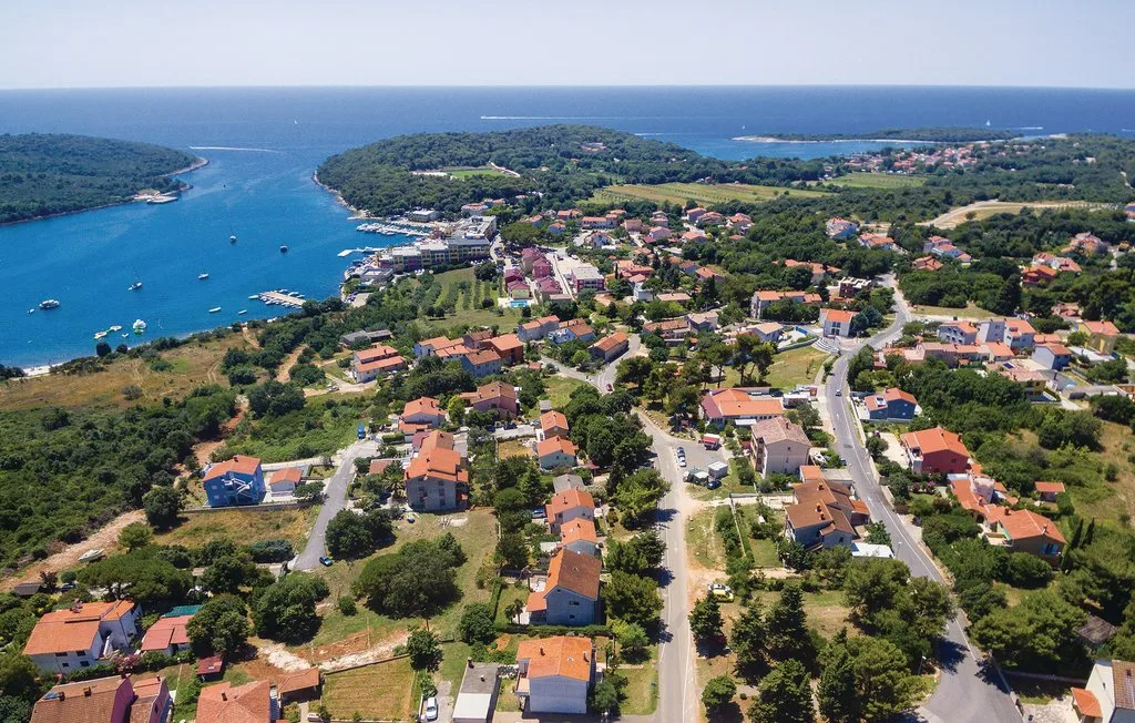 Vista aérea de un pueblo costero, con casas y caminos junto a una bahía azul.